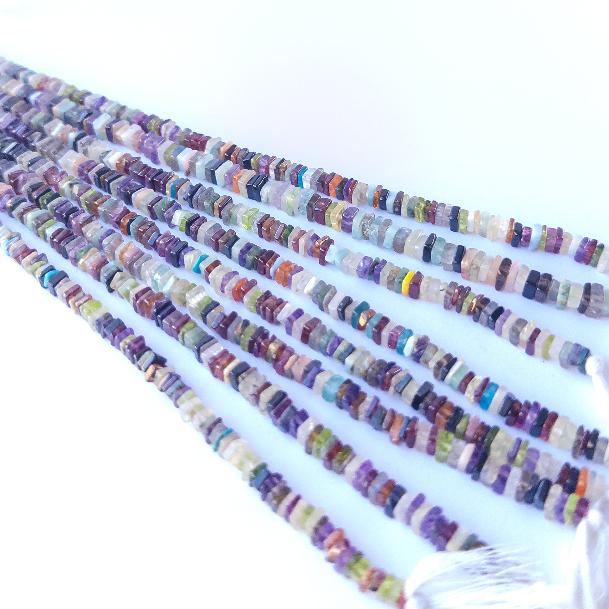 A person holds delicate strands of Disco beads, showcasing their square heishi design.