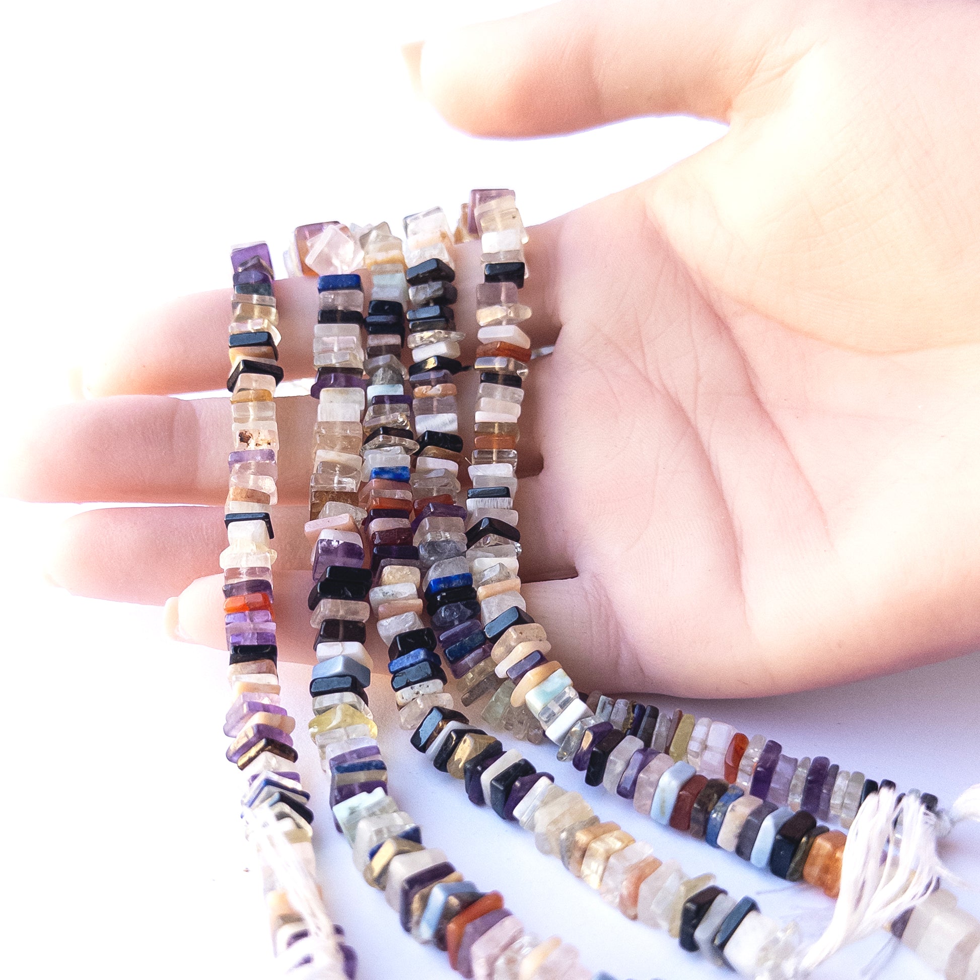 A person holds delicate strands of Disco beads, showcasing their square heishi design.