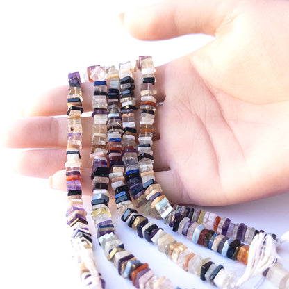 A person holds delicate strands of Disco beads, showcasing their square heishi design.