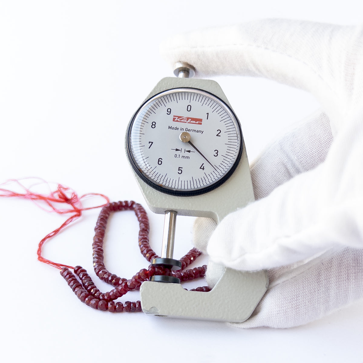 A dial gauge measures the dyed Ruby faceted rondelle 3.6–5mm gemstone.