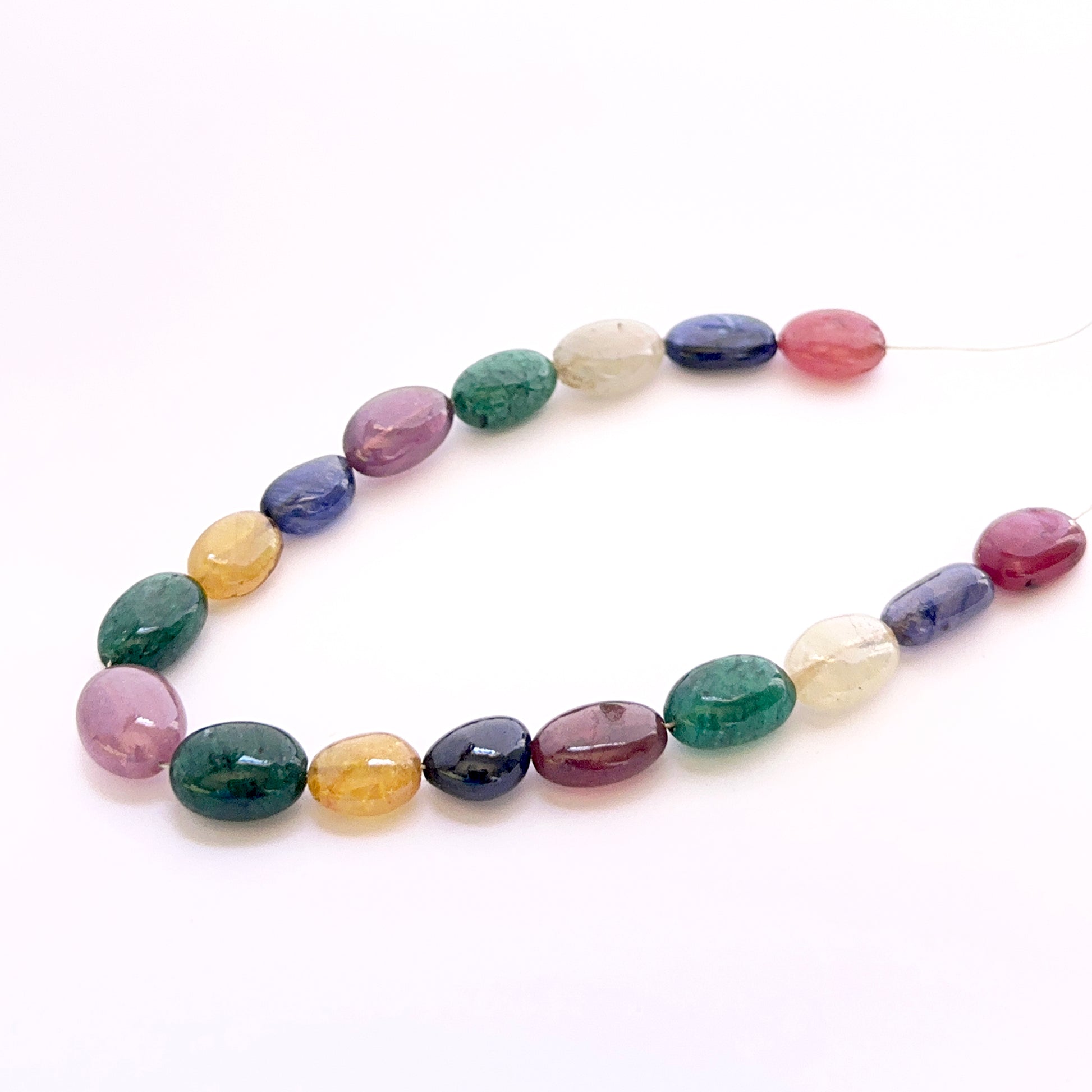 Close‑up of mixed yellow sapphire, ruby, blue sapphire and emerald smooth oval beads showing polished surfaces and vivid colours