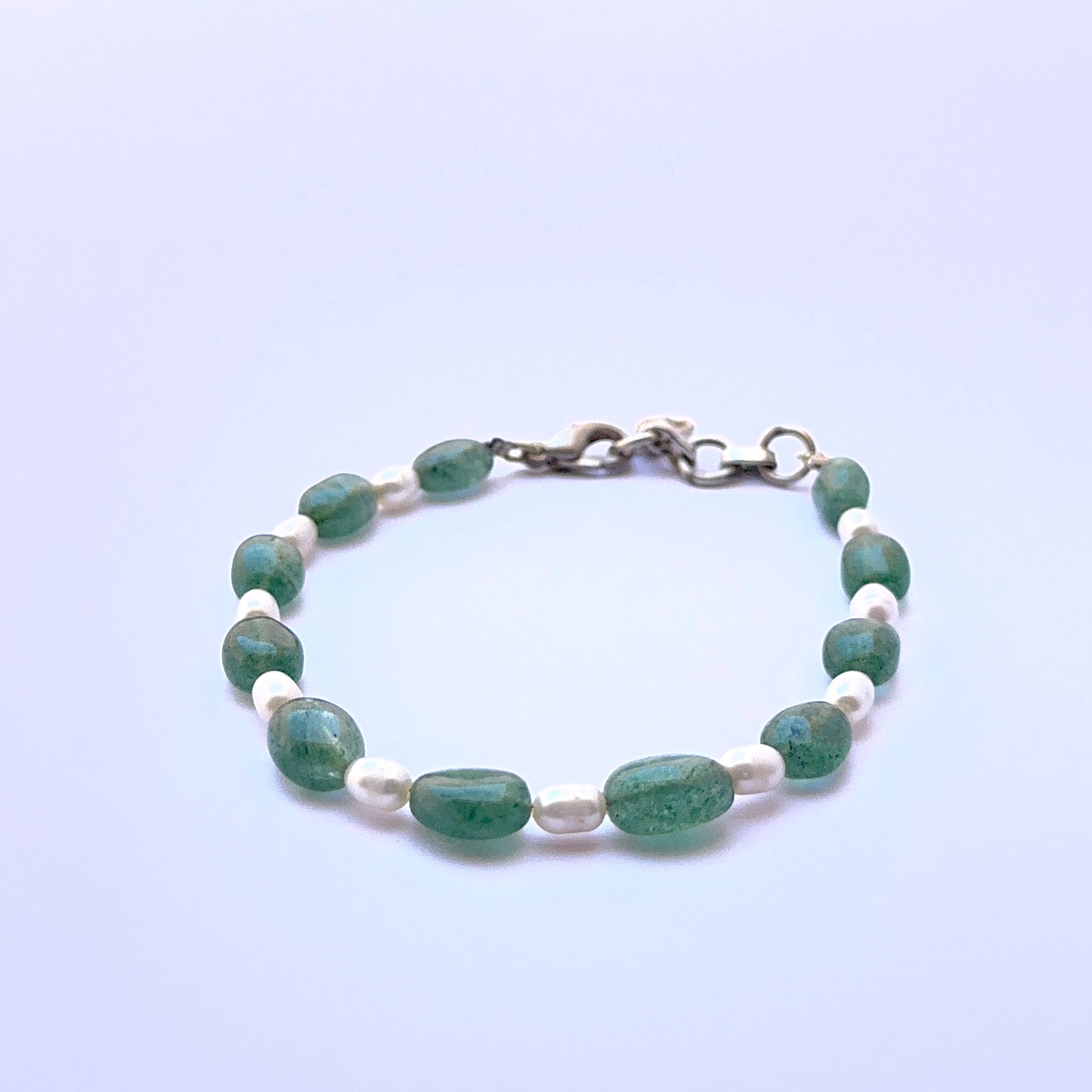 Close‑up of emerald and pearl beads arranged on a polished bracelet.