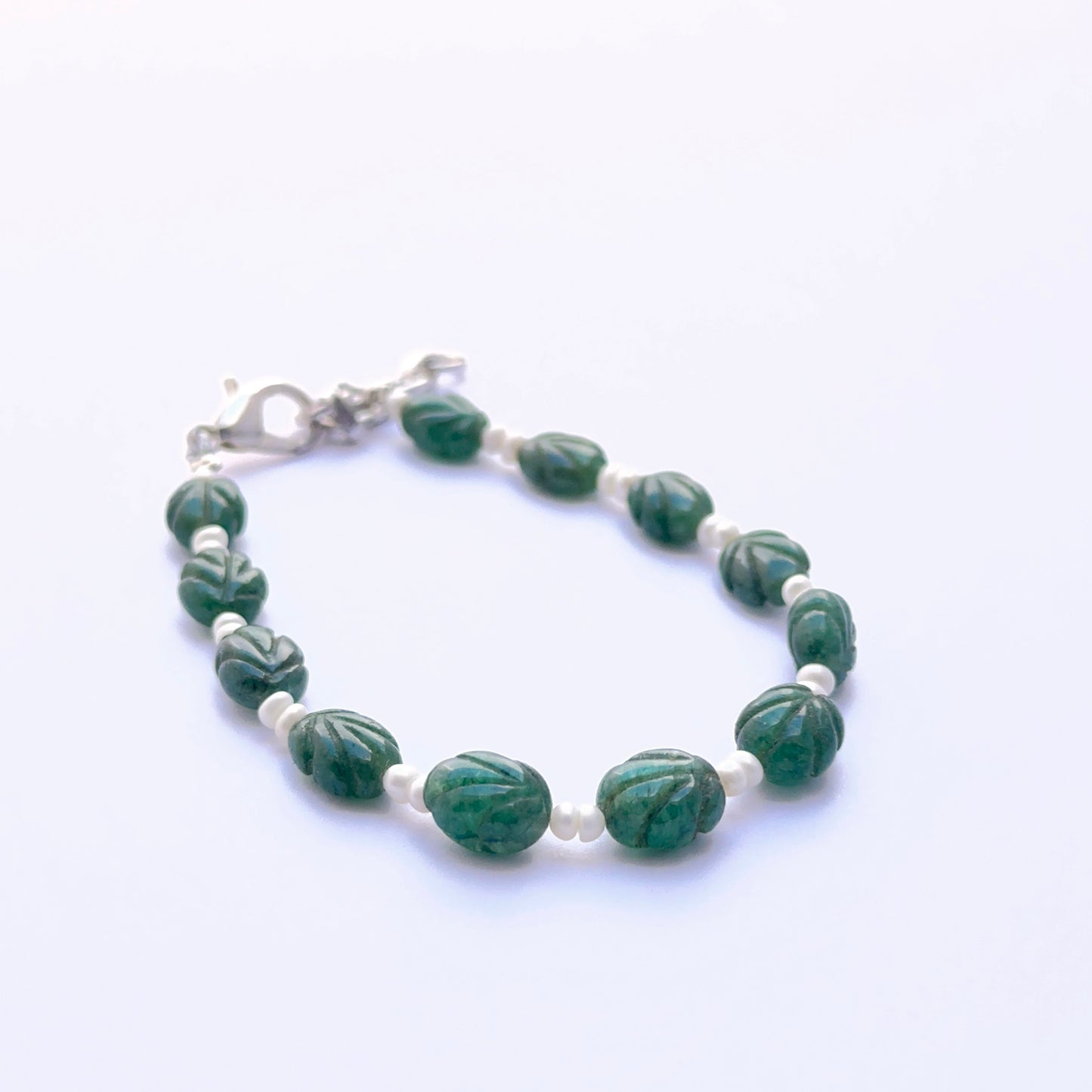 Close‑up of carved emerald and pearl beads arranged on a finished bracelet.
