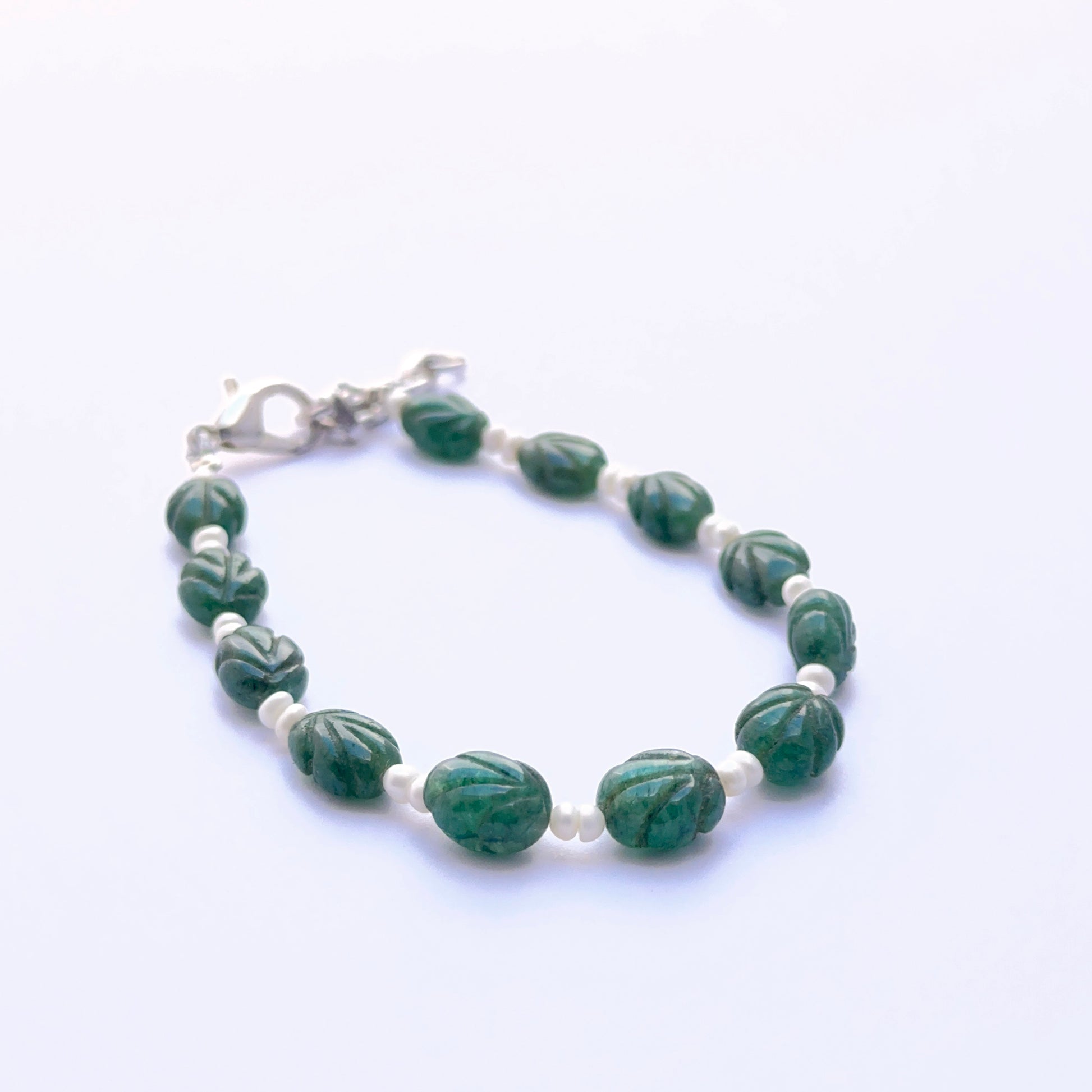 Close‑up of carved emerald and pearl beads arranged on a finished bracelet.