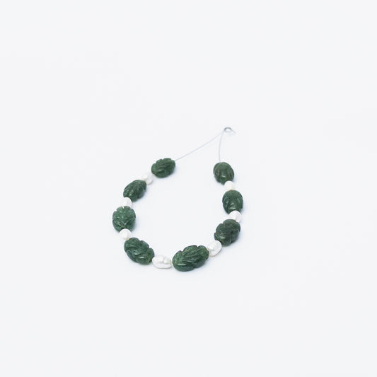 Emerald and Freshwater Pearl carved beads arranged together, showcasing rich green tones and soft pearly shine.