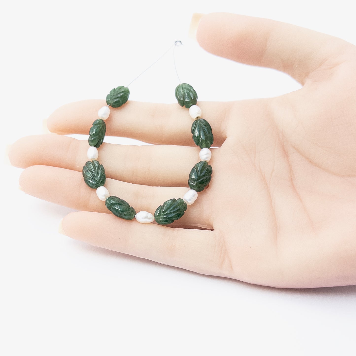 A person holds delicate pieces of Emerald and Freshwater Pearls beads, showcasing their carved design.