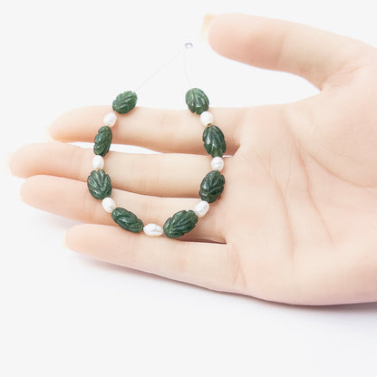 A person holds delicate pieces of Emerald and Freshwater Pearls beads, showcasing their carved design.