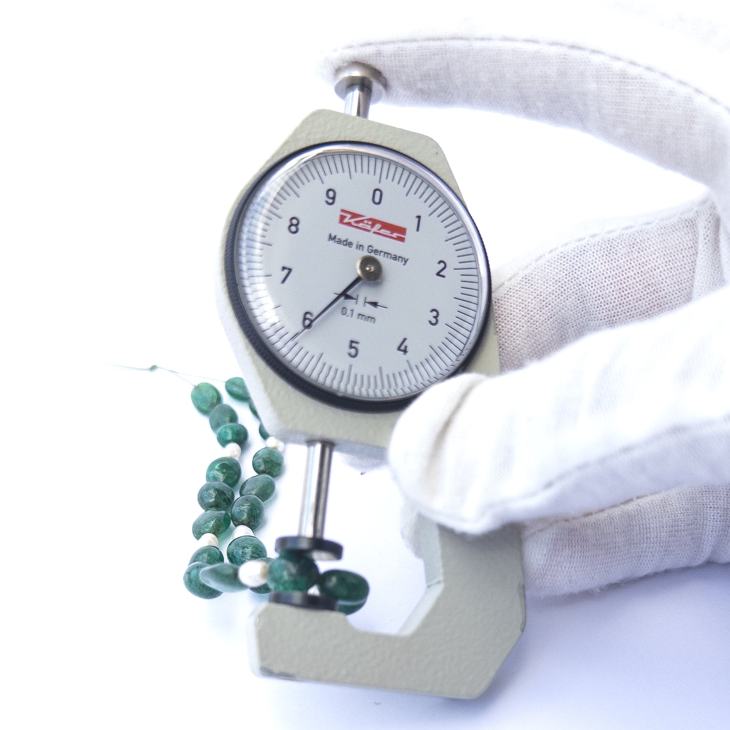 A dial gauge measures the Emerald smooth oval 5.5–7mm gemstone.