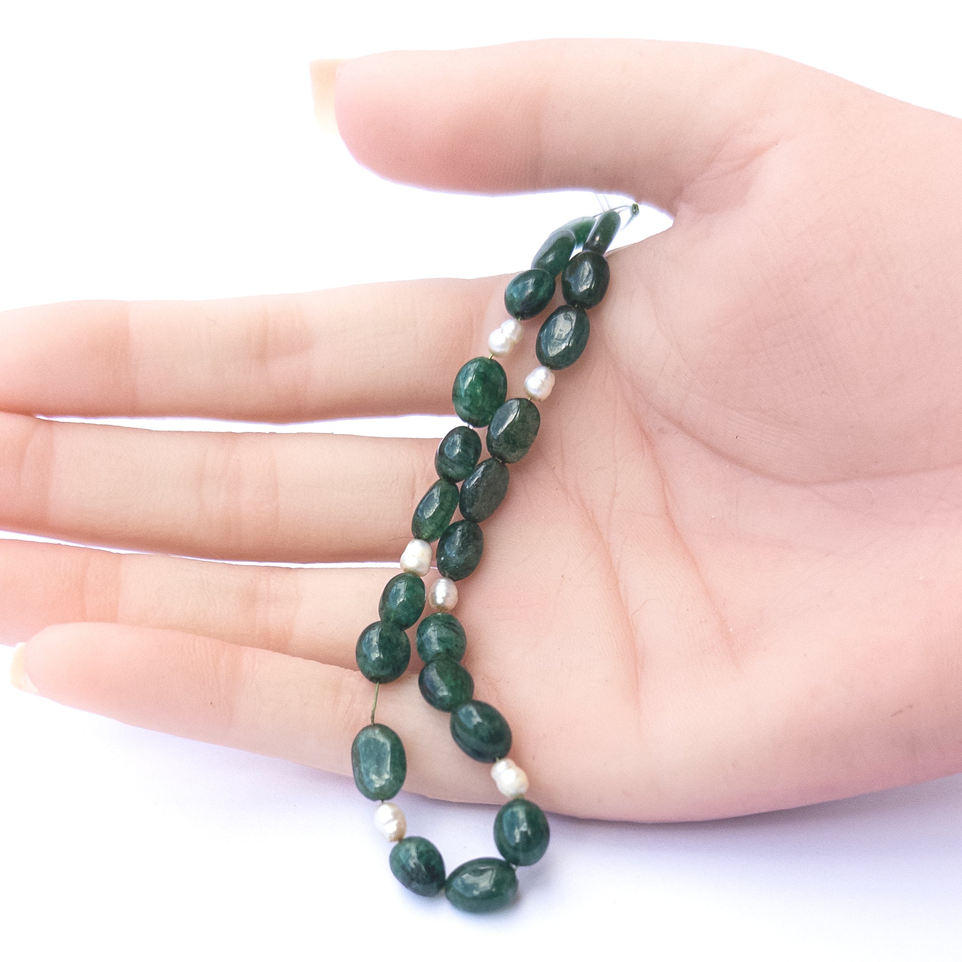 A person holds delicate strands of Emerald and freshwater pearl smooth oval beads, showcasing their polished design.