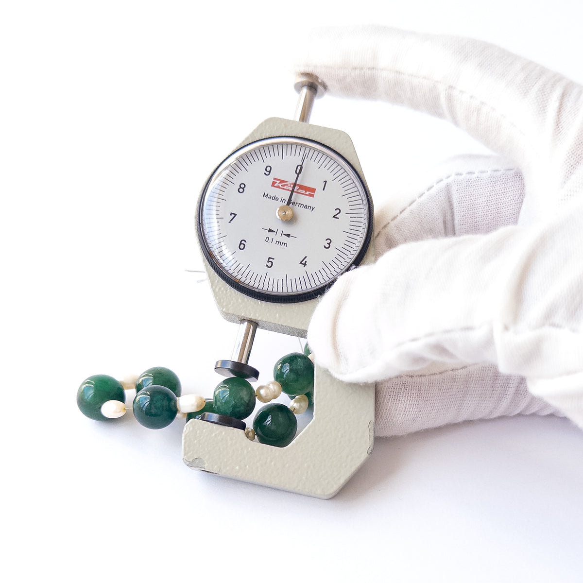 A dial gauge measures the Emerald smooth round 10–11mm gemstone.