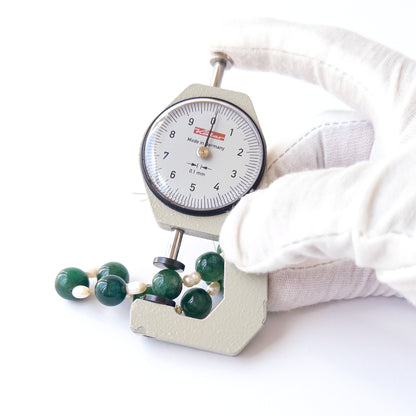 A dial gauge measures the Emerald smooth round 10–11mm gemstone.