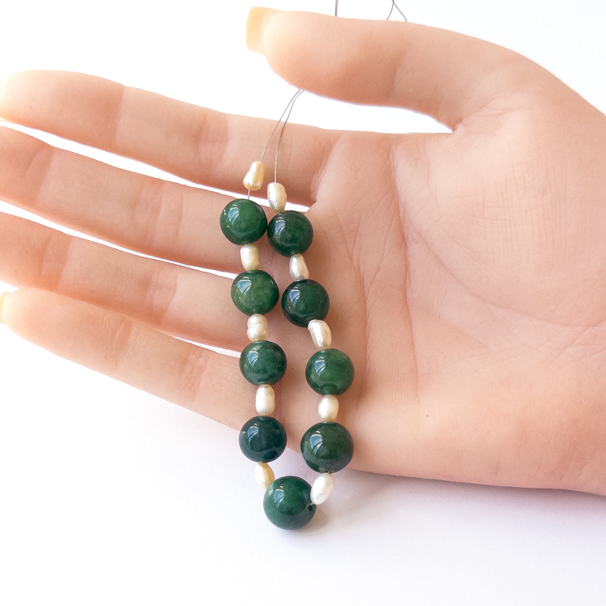 A person holds delicate strands of Emerald and Freshwater Pearl beads, showcasing their smooth round design.