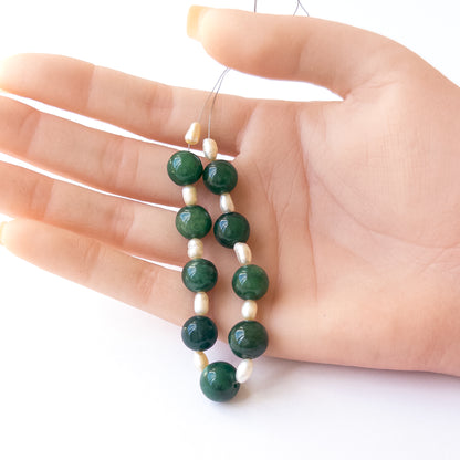 A person holds delicate strands of Emerald and Freshwater Pearl beads, showcasing their smooth round design.