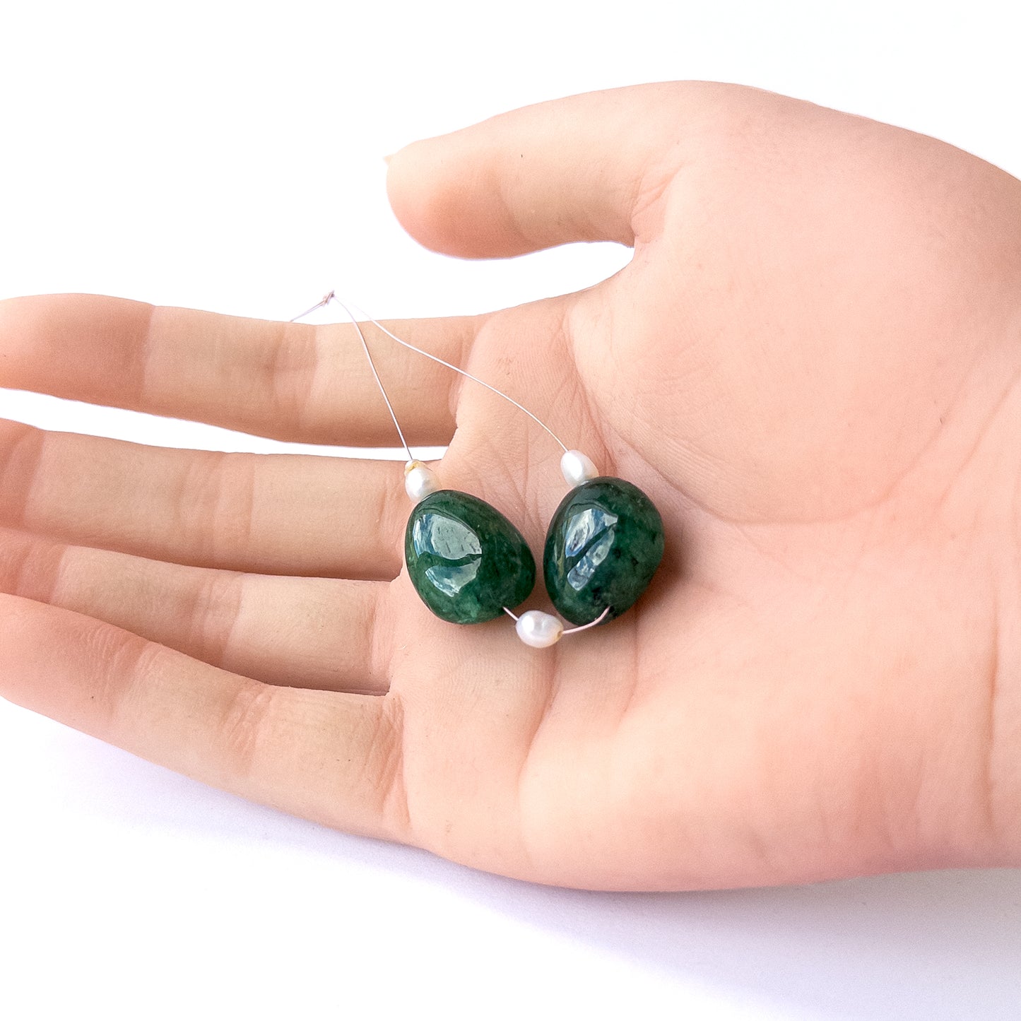 A person holds delicate strands of Emerald and freshwater pearl smooth tumble beads, showcasing their polished design.