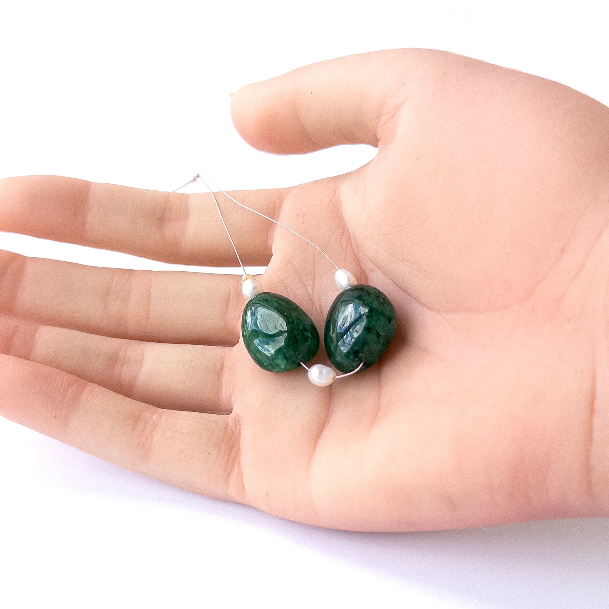 A person holds delicate strands of Emerald and freshwater pearl smooth tumble beads, showcasing their polished design.