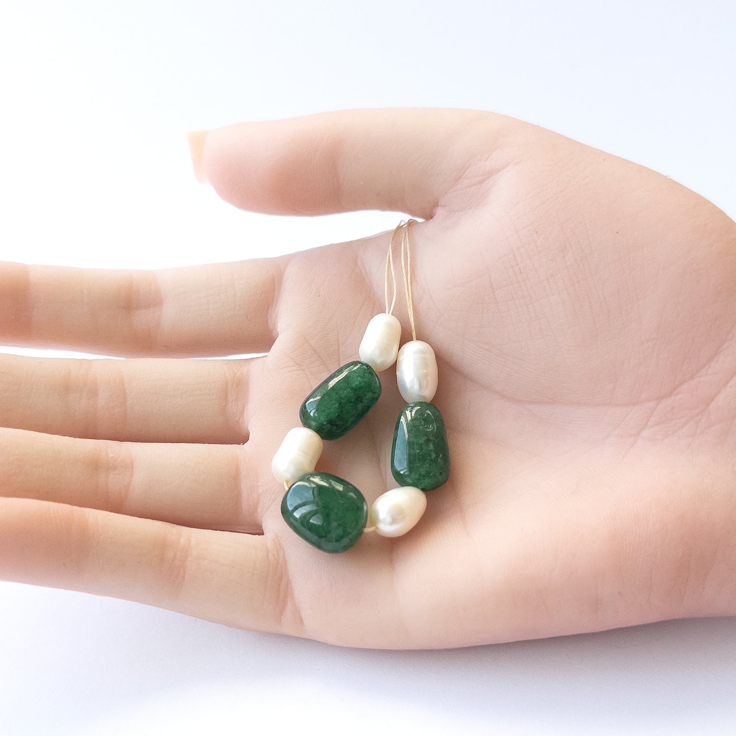 A person holds delicate pieces of Emerald and freshwater pearl beads, showcasing their smooth tumble design.