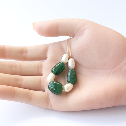 A person holds delicate pieces of Emerald and freshwater pearl beads, showcasing their smooth tumble design.