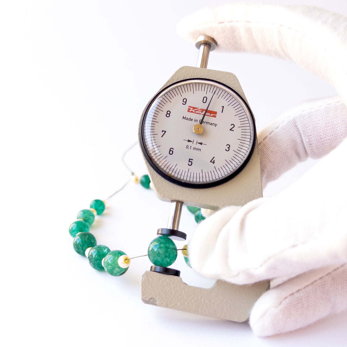A dial gauge measures the Emerald and Shell Pearl smooth round 7.5–10.2mm gemstone.