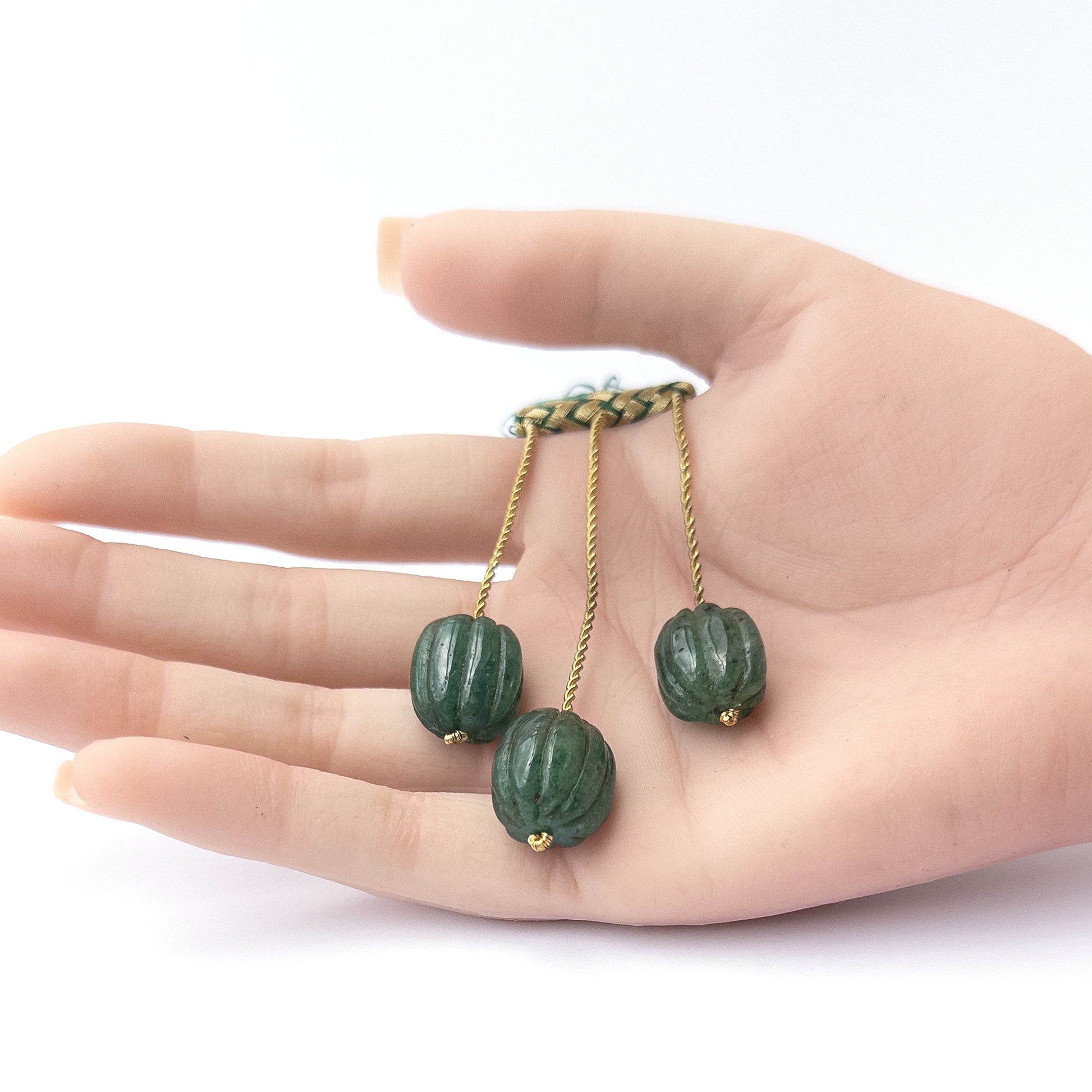 A person holds delicate pieces of Emerald beads, showcasing their carved oval design.
