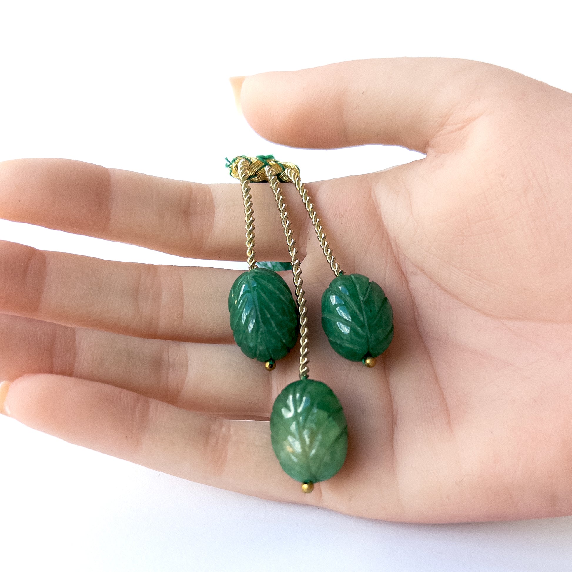 A person holds delicate pieces of Emerald beads, showcasing their carved oval design.