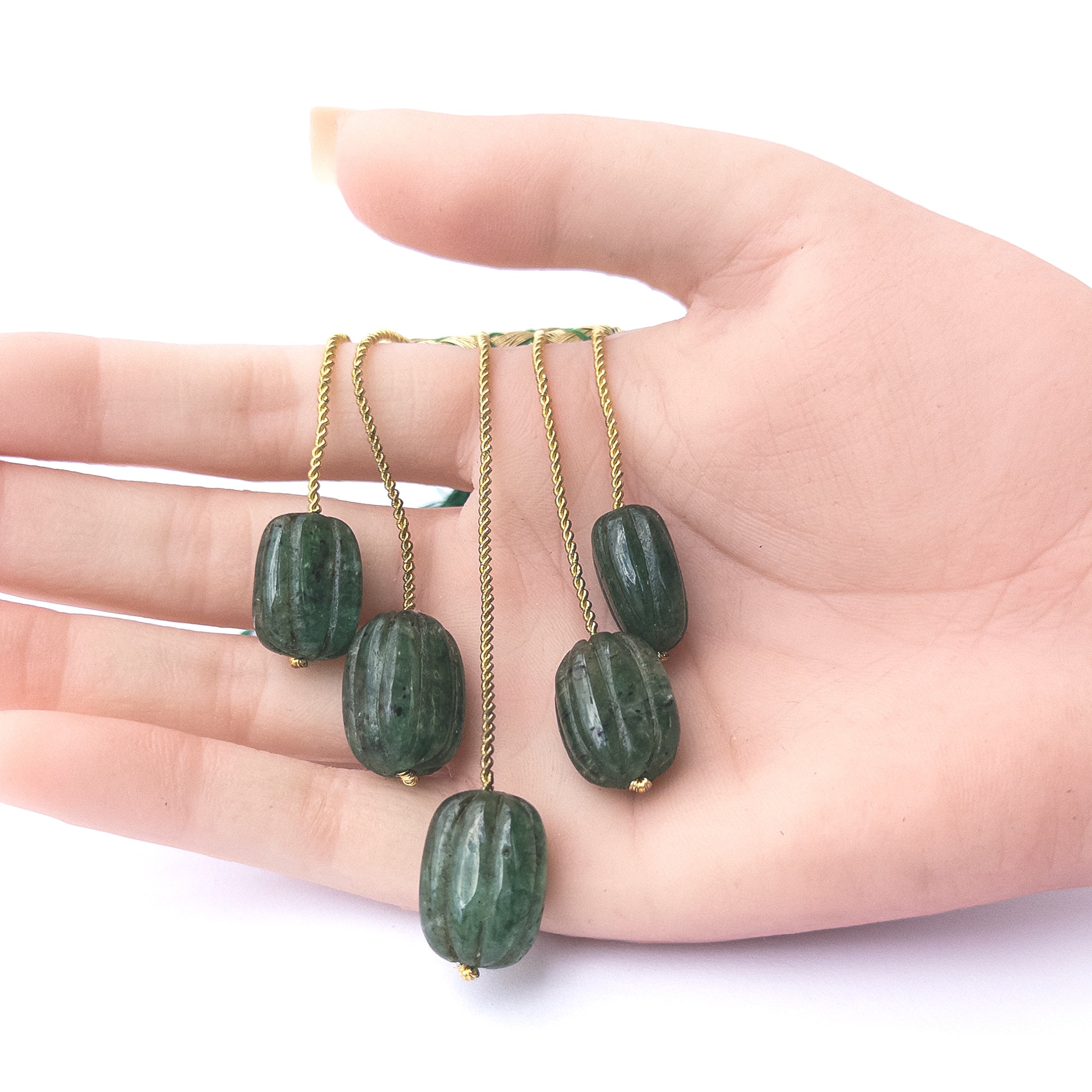 A person holds delicate pieces of Emerald beads, showcasing their carved oval design.