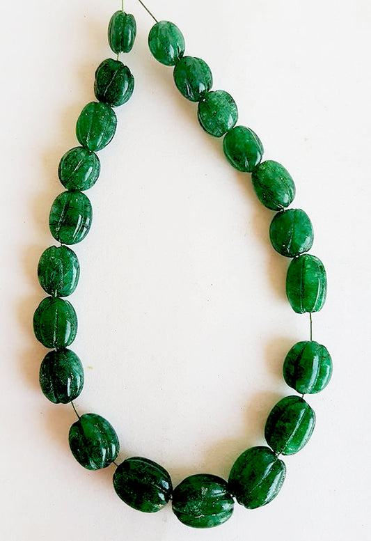 Carved oval emerald beads with rich green hues and intricate detailing, arranged in a symmetrical strand.