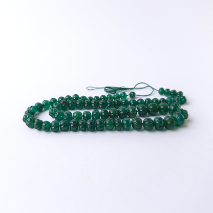 Close up of Emerald gemstone beads showing carved pumpkin cuts and deep green tones for crafting projects.
