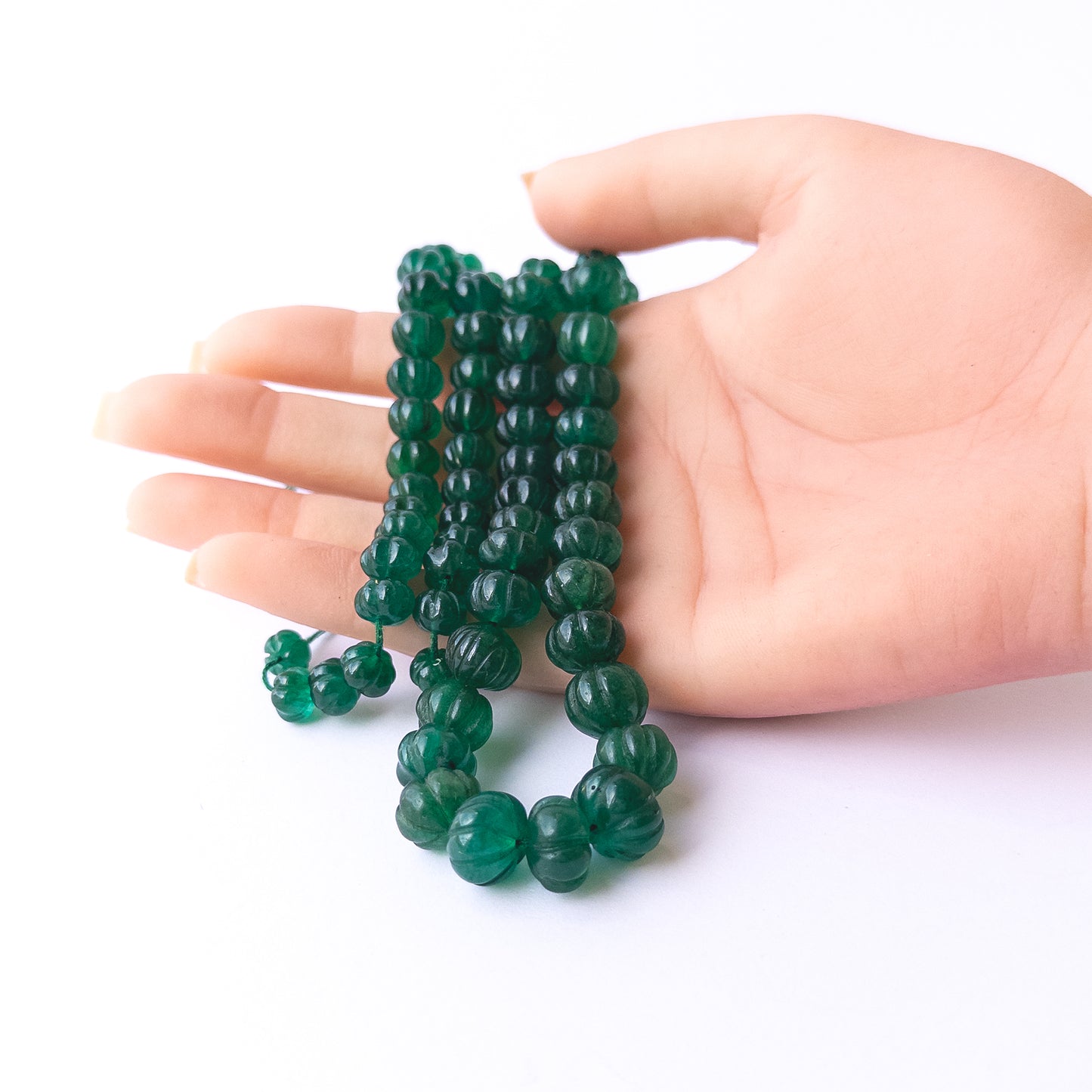 A person holds delicate strands of Emerald beads, showcasing their carved pumpkin design.