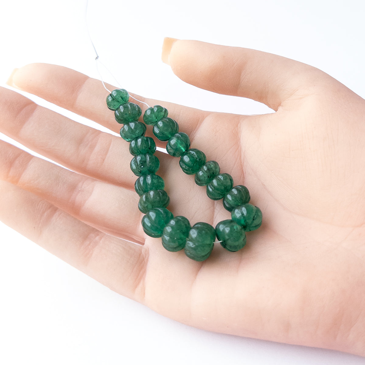 A person holds delicate pieces of Emerald beads, showcasing their carved pumpkin design.