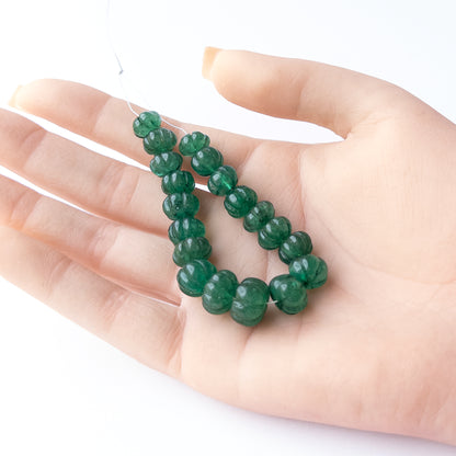 A person holds delicate pieces of Emerald beads, showcasing their carved pumpkin design.