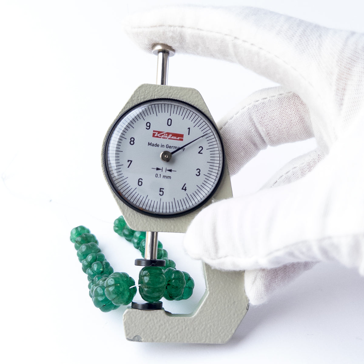 A dial gauge measures the Emerald Carved Pumpkin 8.5-11mm gemstone.