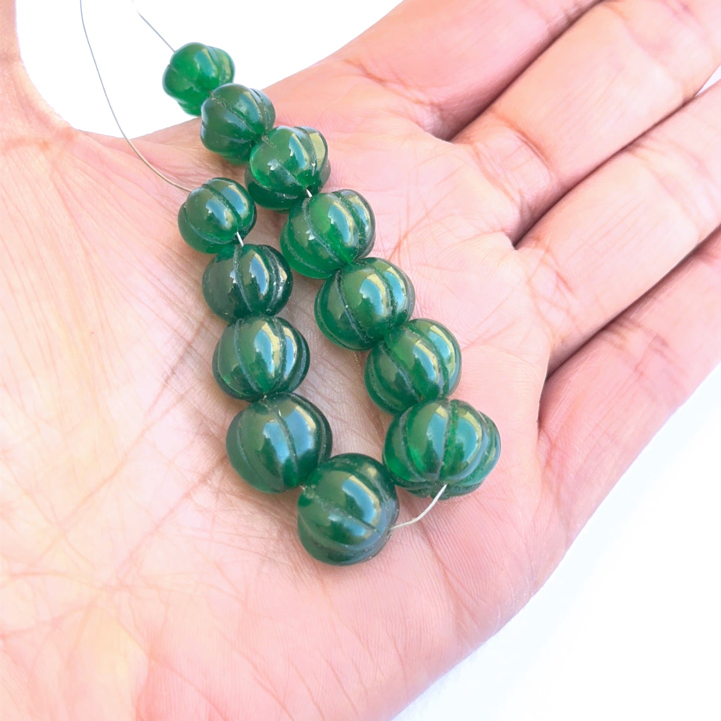 A person holds delicate strands of emerald beads, showcasing their smooth design. 