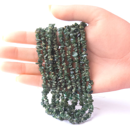 A person holds delicate strands of Shaded Emerald chip beads, showcasing their organic design.