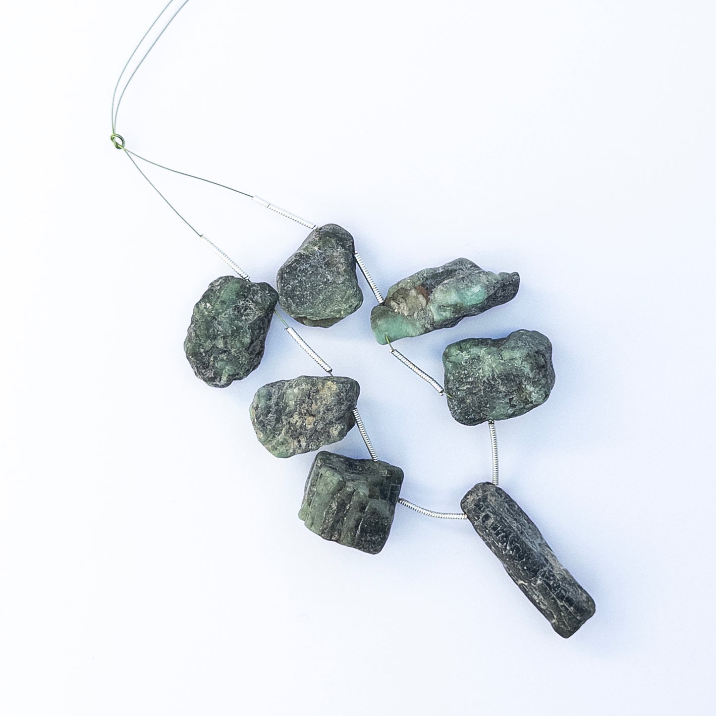 Emerald drilled rough gemstone pieces arranged together, showcasing deep green tones and natural raw texture.