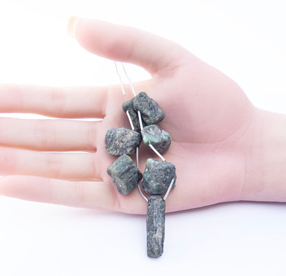 A person holds delicate pieces of Emerald rough beads, showcasing their drilled rough design.