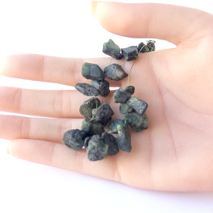 A person holds delicate pieces of Emerald rough beads, showcasing their drilled rough design.