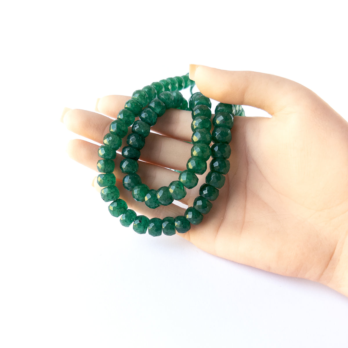 A person holds delicate strands of Emerald beads, showcasing their faceted rondelle design.