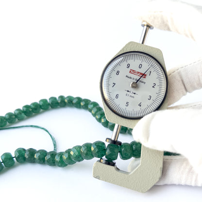 A dial gauge measures the Emerald faceted rondelle 9–11.5mm gemstone.