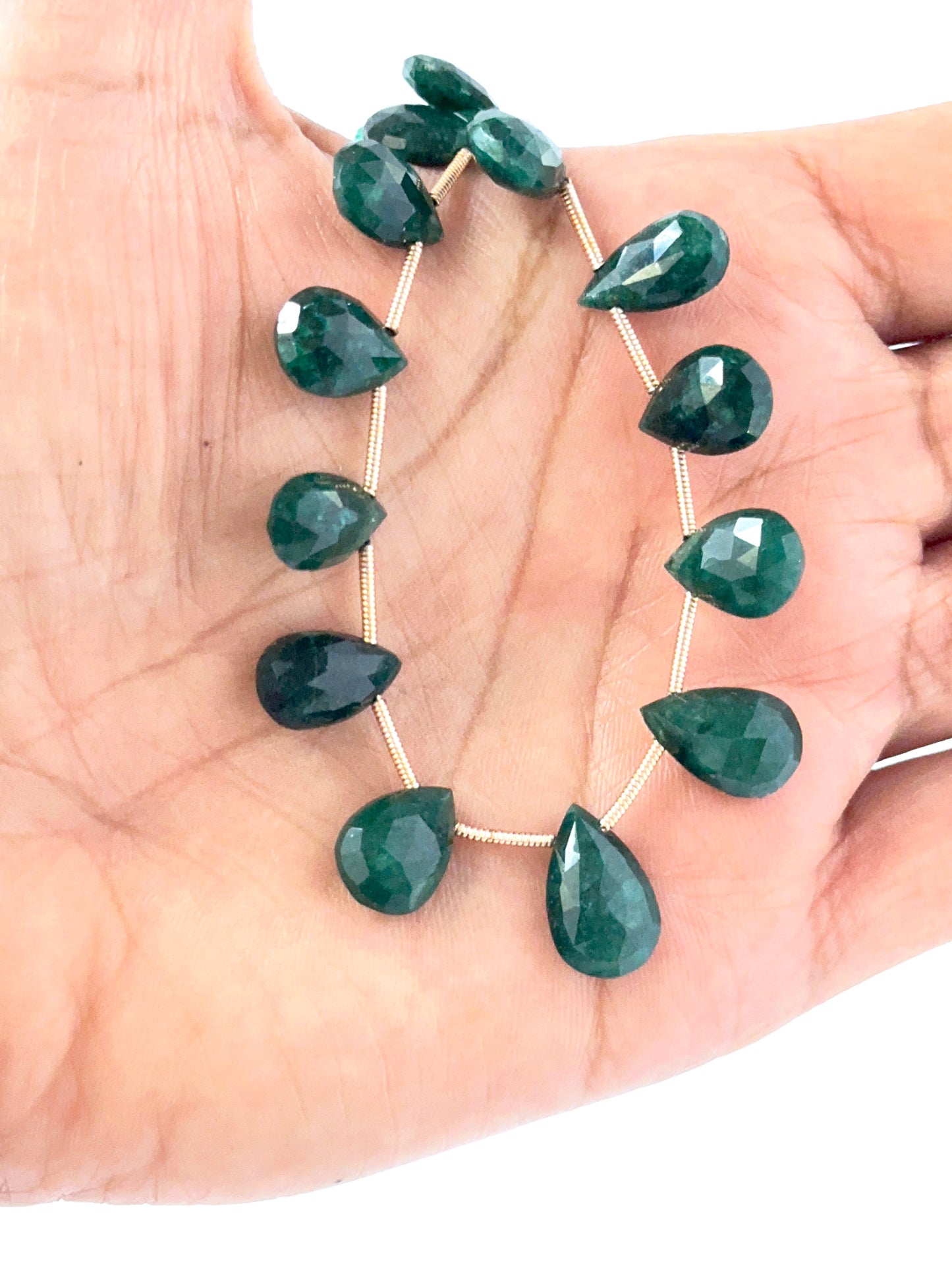A person holds delicate strands of Emerald beads, showcasing their smooth design.
