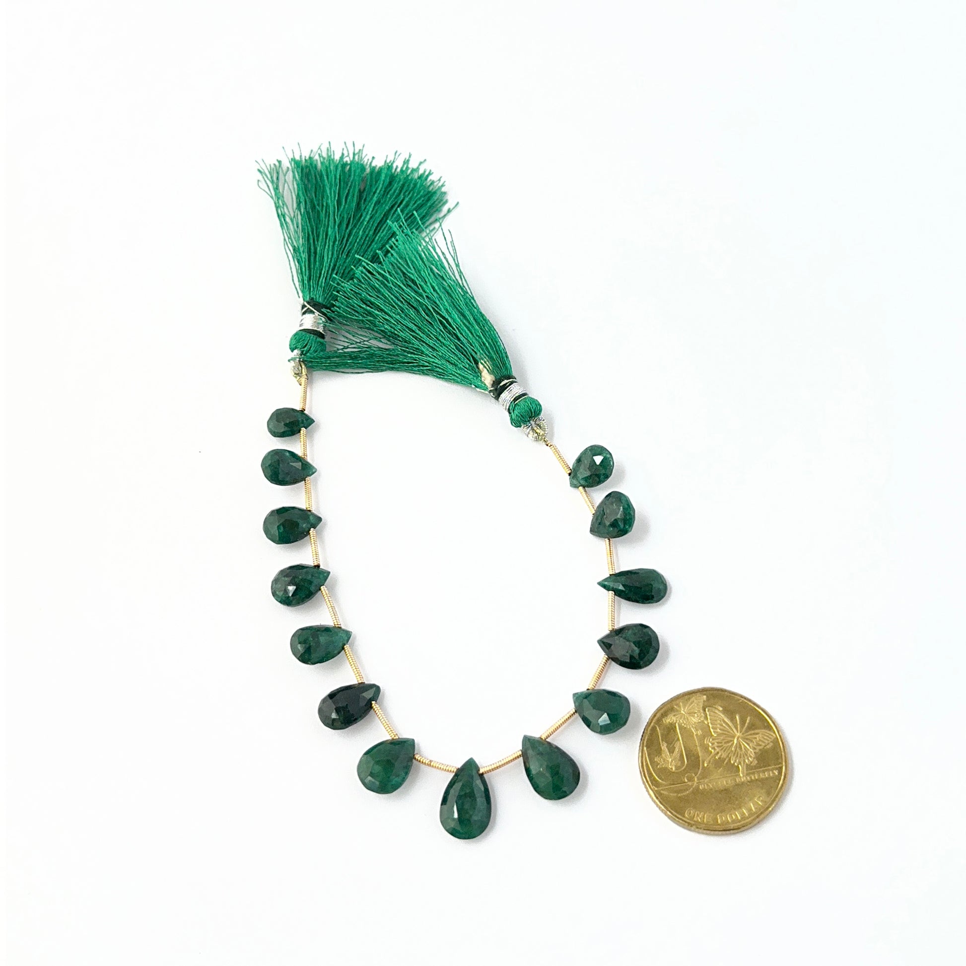 Australian dollar coin place next to the Emerald faceted teardrop 9.5–14mm gemstone to show scale.