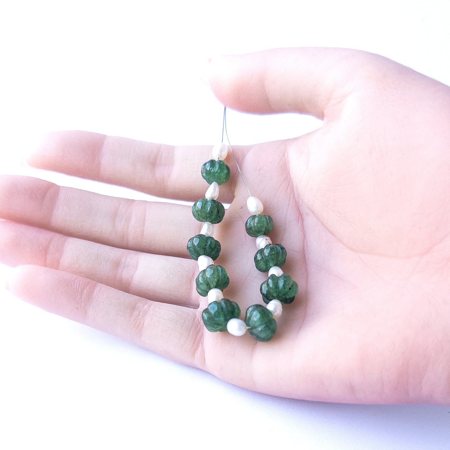 A coin is placed near delicate pieces of Emerald and Freshwater Pearl beads for scale.