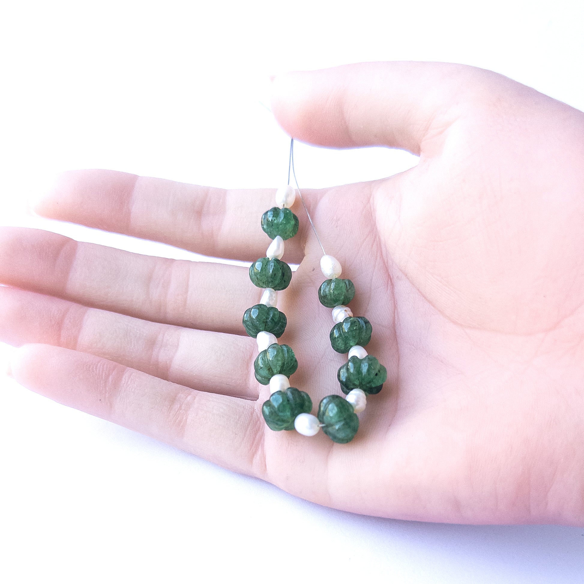 A coin is placed near delicate pieces of Emerald and Freshwater Pearl beads for scale.