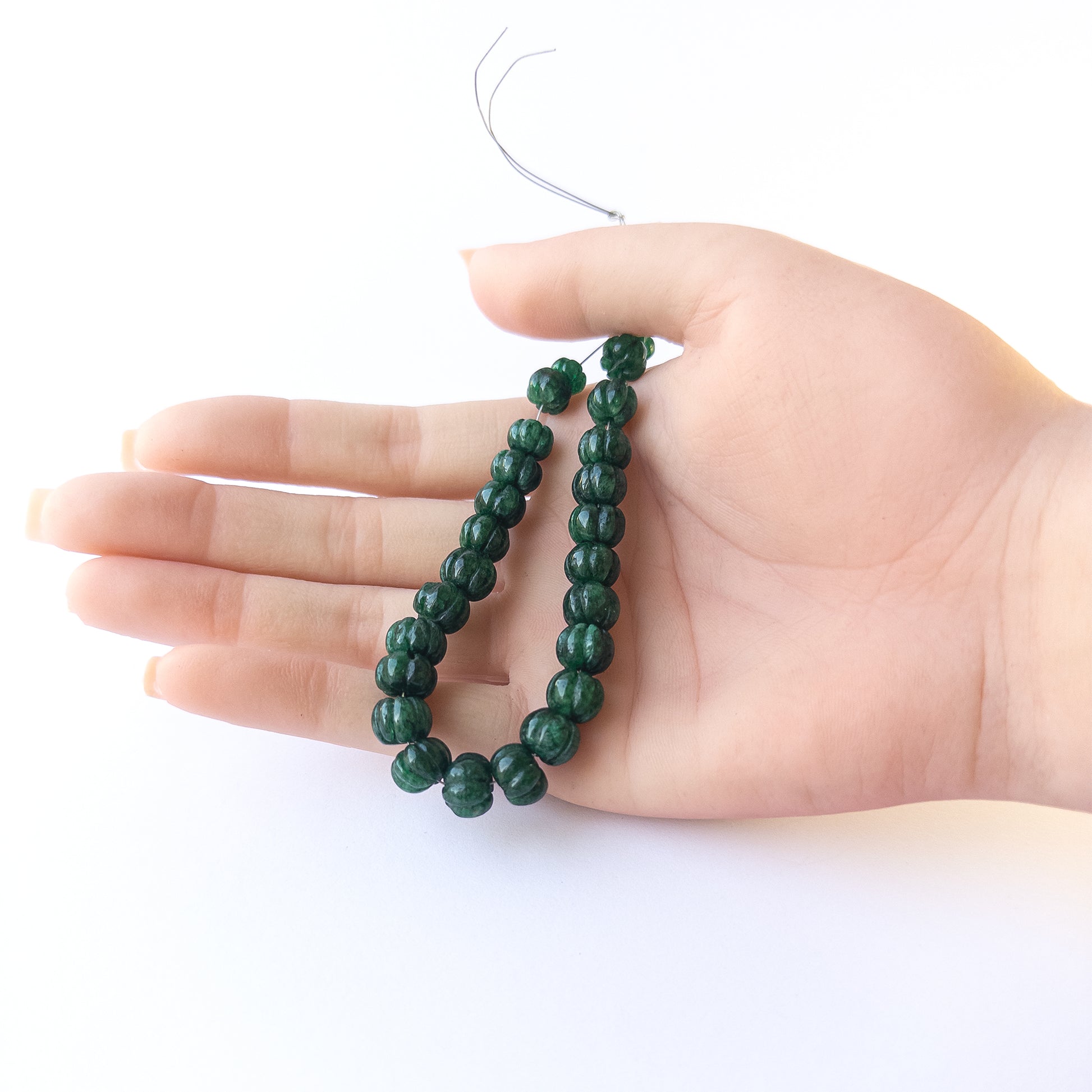 A person holds delicate strands of Emerald beads, showcasing their pumpkin‑cut design.  