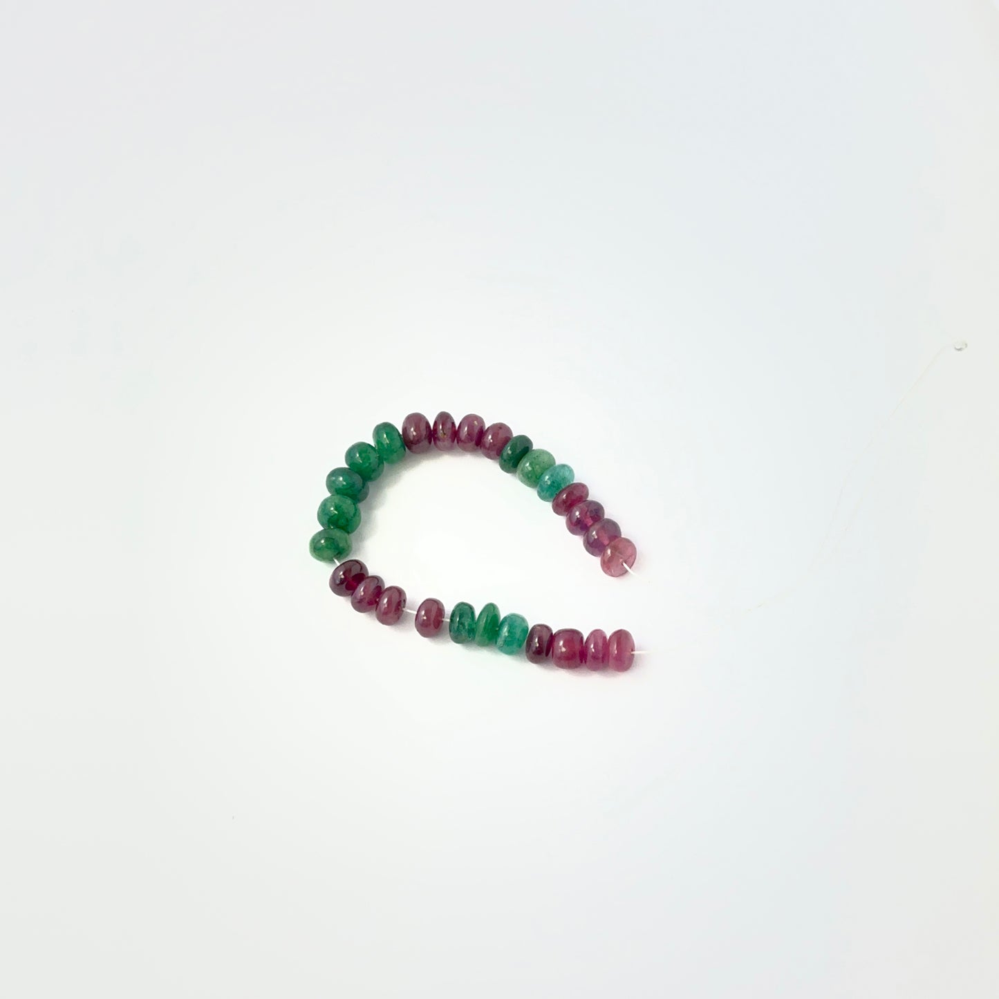 Close view of Emerald and Ruby smooth rondelles arranged as 27 pieces for handmade jewellery components.