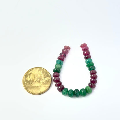 A coin is place near delicate pieces of Emerald and Ruby beads for scale.