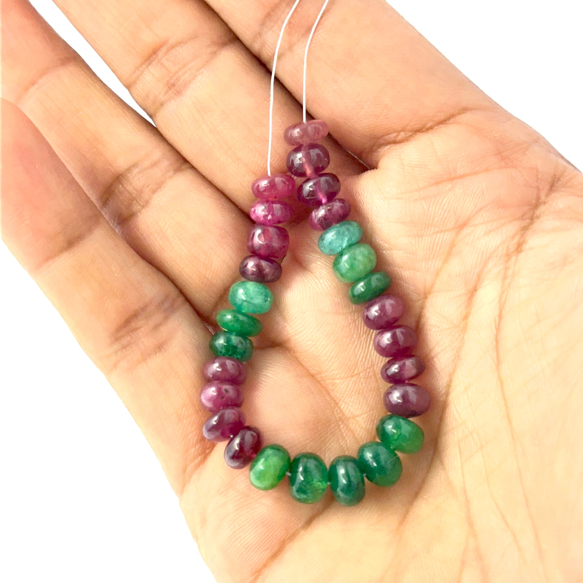 A person holds delicate strands of Emerald and Ruby beads, showcasing their smooth rondelle design.
