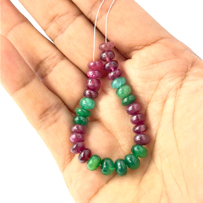 A person holds delicate strands of Emerald and Ruby beads, showcasing their smooth rondelle design.