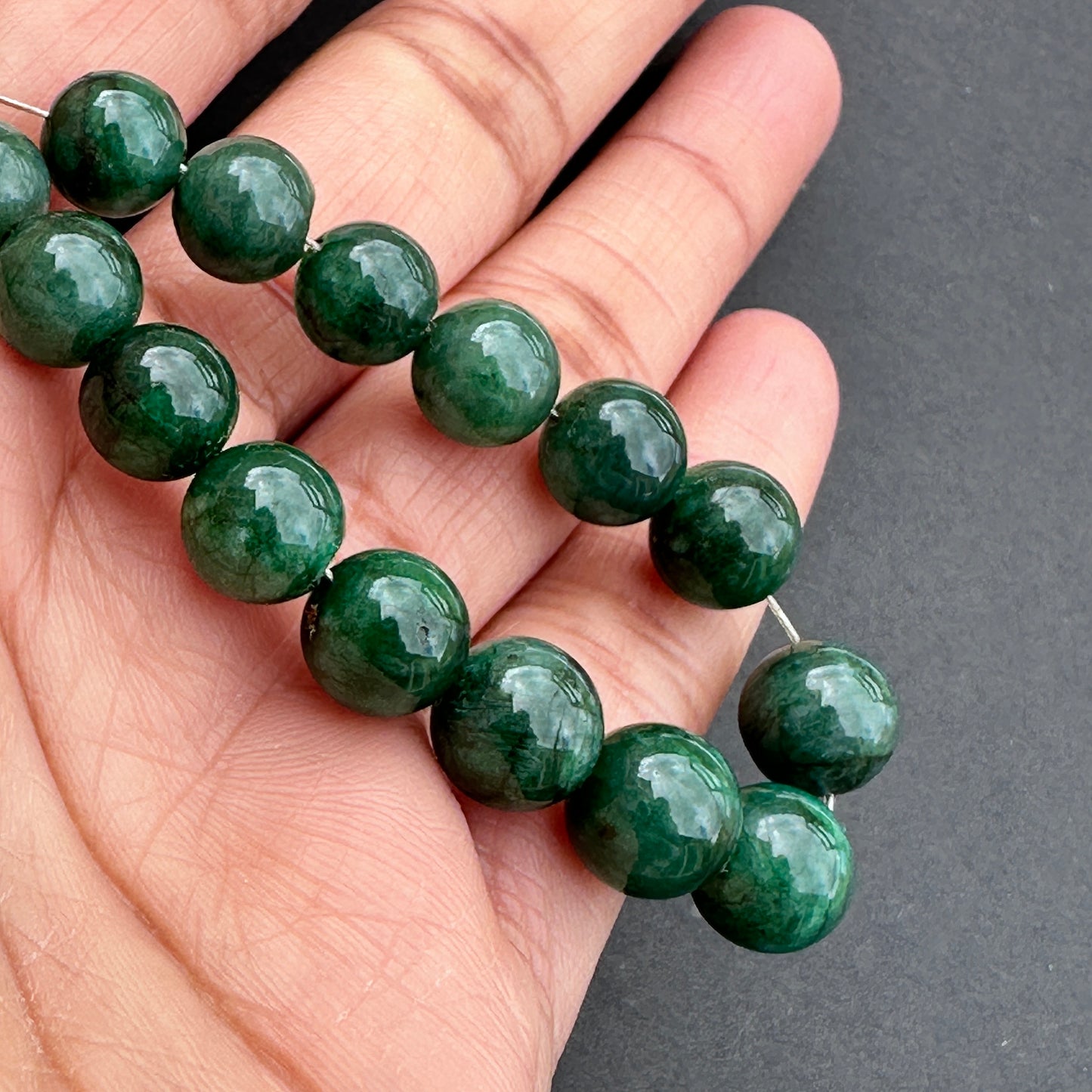 A person holds delicate strands of emerald beads, showcasing their smooth design.