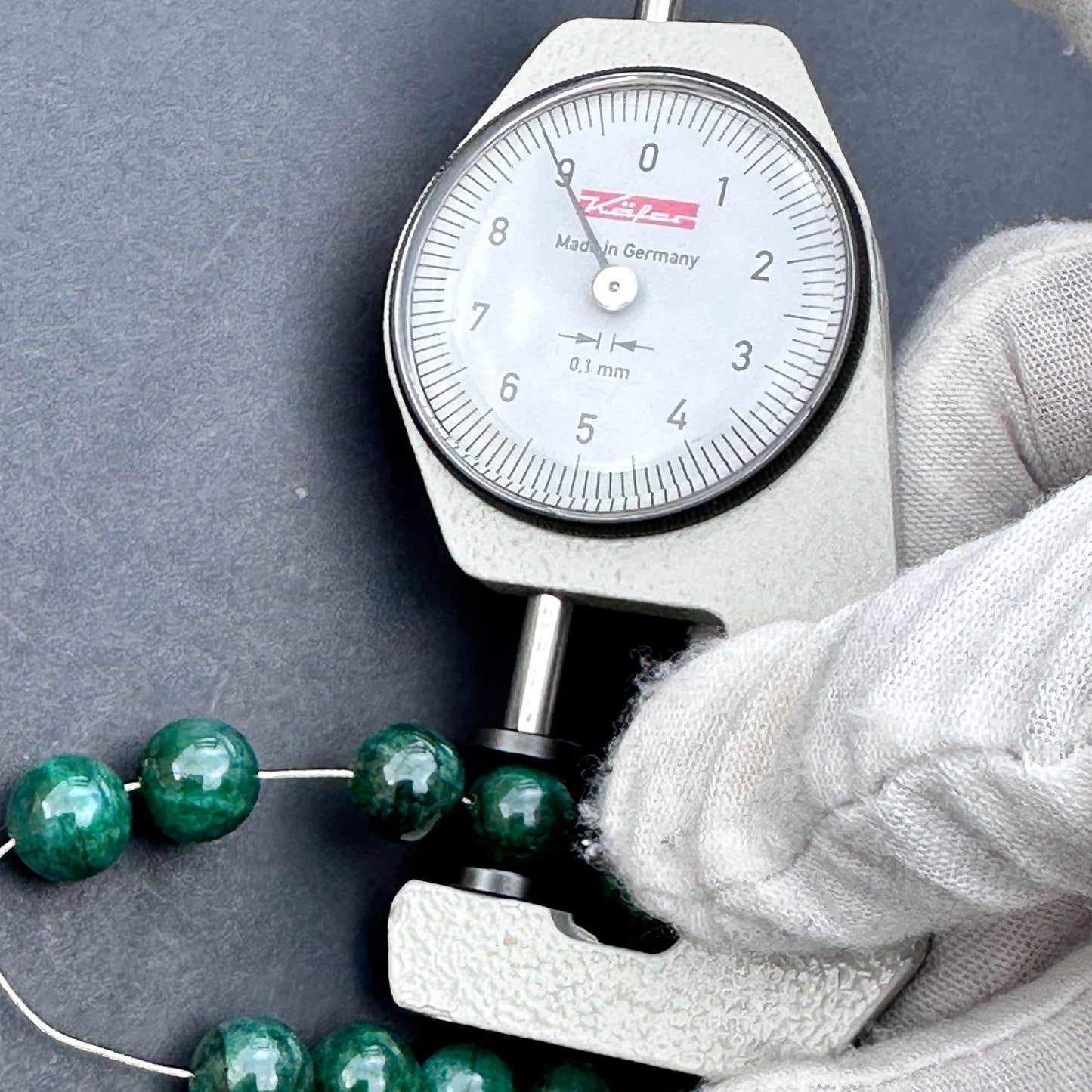 A dial gauge measures the emerald rondelle 9mm gemstone.