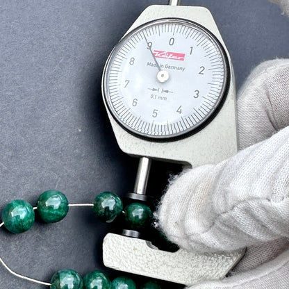 A dial gauge measures the emerald rondelle 9mm gemstone.